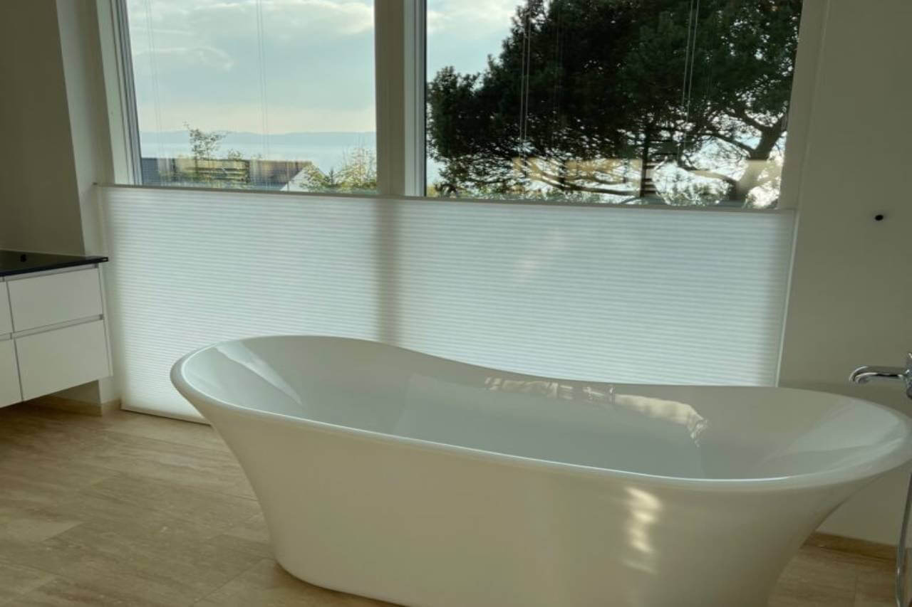 Hvide plisségardiner på badeværelse med et badekar i forgrunden